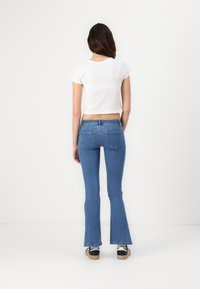 Camiseta blanca corta con mangas cortas, combinada con jeans azules acampanados. Los jeans tienen una cintura alta y dos bolsillos traseros. Calzado casual visible.