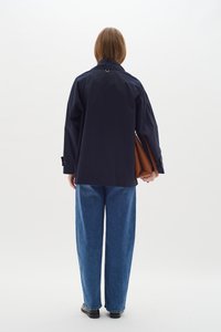 Jūras zila ūdensnecaurlaidīga jaka ar brīvu piegriezumu, garām piedurknēm un augstu apkakli. Savienota ar platām zilo džinsu biksēm un turot brūnu somu.