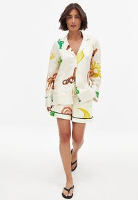 Linnedragt i pyjamas sæt med hvid baggrund og farverige frugt- og havdyrsmønstre; inkluderer en skjorte med knapper og shorts med piping.