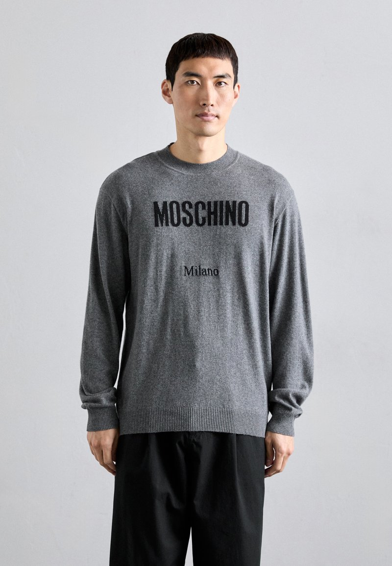 Pilkas megztinis su ilgomis rankovėmis, priekyje juodai spausdinta "MOSCHINO" ir "Milano". Klasikinis apvalus iškirpimas ir dryžuota apačia.