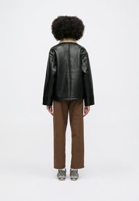 Czarna skórzana kurtka z futrzanym kołnierzem, szerokimi rękawami i prostym krojem; noszona z brązowymi spodniami i szarymi trampkami.