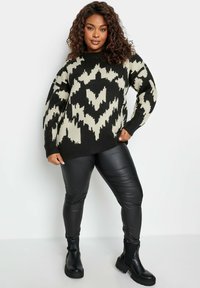 Maglione lavorato a maglia nero e crema con un design oversize, abbinato a pantaloni in eco-pelle neri e stivaletti alla caviglia.