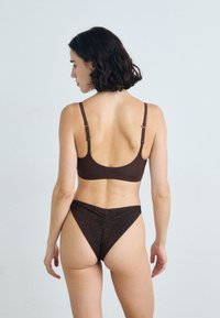 Haut de bikini marron avec bretelles réglables, associé à un bas taille haute dans une texture sombre et scintillante. La vue arrière met en avant les détails de conception.