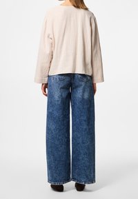 Maglietta a maniche lunghe di un rosa chiaro e testurizzata abbinata a jeans in denim blu a gamba larga. La maglietta ha una vestibilità rilassata e un collo rotondo.