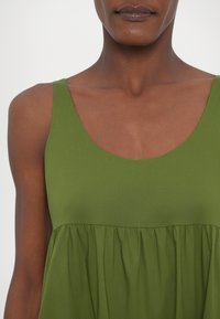 Abito verde senza maniche con scollatura a barchetta e corpetto arricciato. Tessuto liscio, lunghezza al ginocchio con vestibilità comoda.
