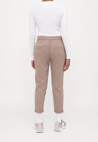 Pantalons texturés marron clair avec taille élastique et ourlets retroussés, associés à des baskets blanches avec des accents beiges et gris.