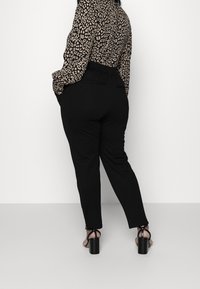 Un pantalon noir à la coupe ajustée, avec une texture lisse et des poches latérales, associé à un chemisier à imprimé léopard. Des sandales à talons carrés.