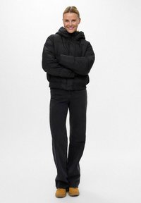 Giacca a vento nera con cappuccio, design cropped e chiusura con zip. Abbinata a jeans scuri e stivaletti beige, per un look casual.