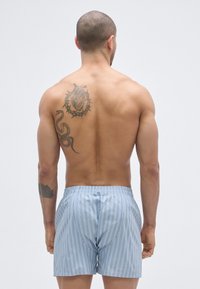 Kék csíkos boxernadrágok rugalmas derékpánttal, könnyű anyagból; egy meztelen hátú modellen, aki egy tetoválást mutat be.