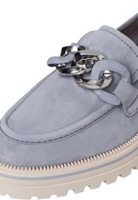 Jasnoniebieskie zamszowe loafery mają masywną srebrną łańcuchową ozdobę oraz beżową gumową podeszwę z fakturowanym wykończeniem.
