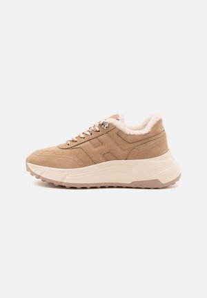 Beige sneaker met dikke witte zool, bontvoering, patroonveters en gestikte zijkanten, getoond vanaf de buitenkant op een effen achtergrond.