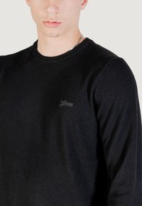 Maglione nero in morbido tessuto, con scollatura rotonda e maniche lunghe. Un piccolo logo ricamato è visibile sul petto.