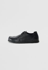 Chaussure en cuir noir à lacets avec un bout arrondi, une surface texturée et une semelle en caoutchouc flexible à bord piqué.