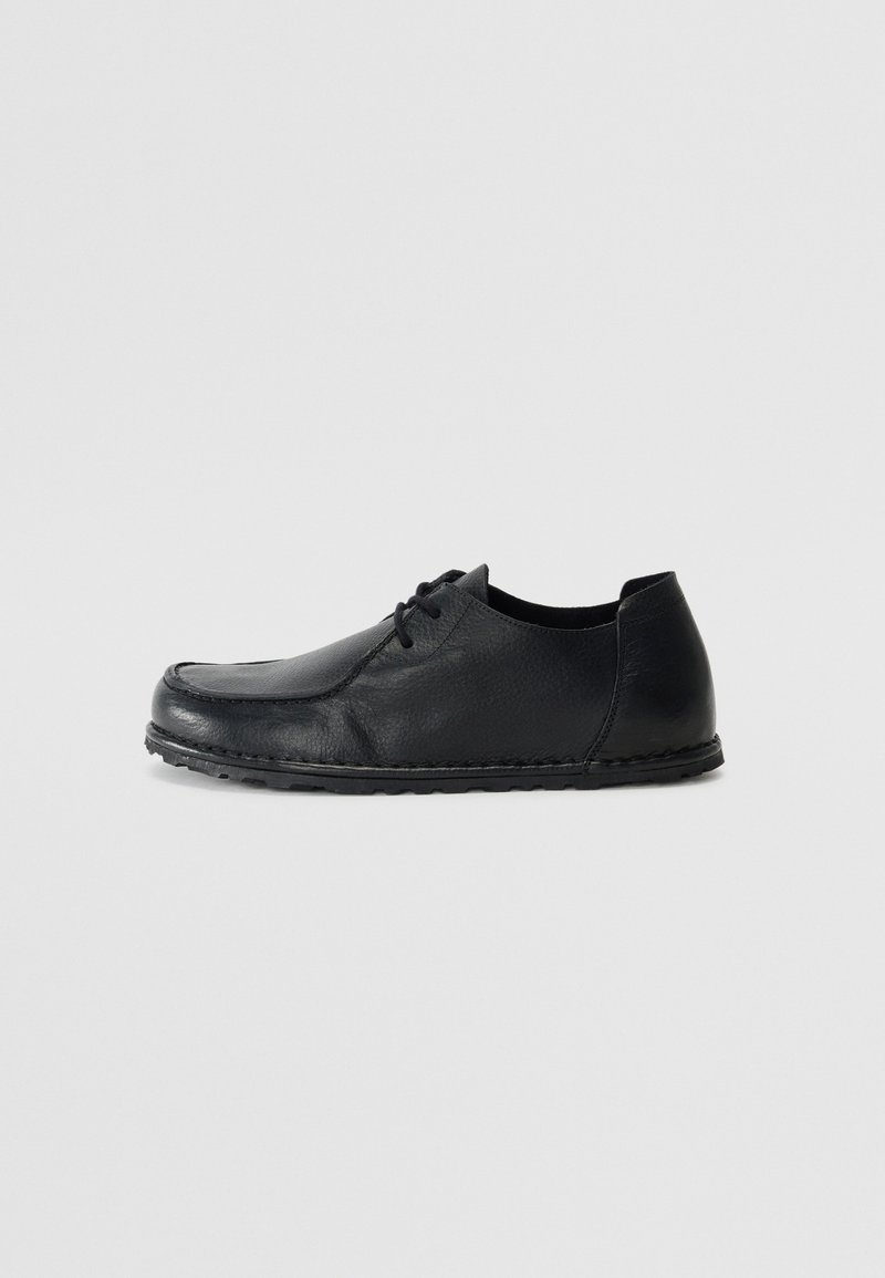 Shoe de couro preto com atacadores, apresentando uma biqueira arredondada, superfície texturizada e uma sola de borracha flexível com um acabamento costurado.