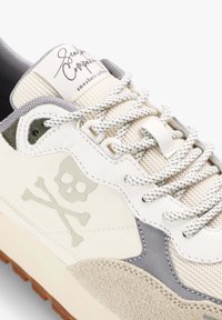 Zapatillas de cuero blanco y ante gris con acentos de malla, cordones estampados y un emblema de calavera translúcido en el costado. Suela ligera.