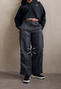 Šedé voděodolné kalhoty s bílými reflexními doplňky, spárované s černou zkrácenou mikinou s předním zipem a detailem loga. Černé tenisky.