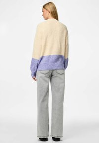 Pull en tricot avec une partie supérieure crème et une partie inférieure lavande. Coupe ample, col rond, et tissu texturé associé à un jean gris taille haute.