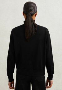 Musta villapaita pitkillä hihoilla, ribbireunuksilla ja helmalla. Pehmeä rakenne, yksinkertainen muotoilu ilman näkyviä kuvioita tai varusteita.