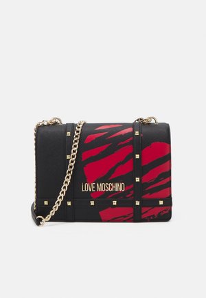Musta-punainen kuviollinen Love Moschino -käsilaukku, jossa on kultaiset niitit ja ketjuhihna valkoisella taustalla.