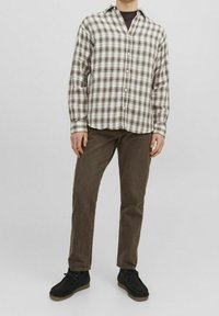 Brun och beige rutigt skjorta med knäppning, långa ärmar, rundad nederkant. Kombinerad med mörkbruna jeans och svarta skor med ljusa sulor.