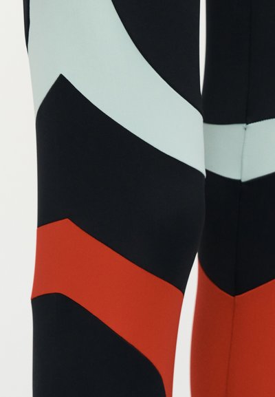 Μαύρο ύφασμα με κυρτές οριζόντιες ρίγες σε ανοιχτό μπλε και κόκκινο χρώμα, σχηματίζοντας ένα μοτίβο που θυμίζει ζιγκ-ζαγκ σε κοντινό τμήμα ενός ενδύματος.