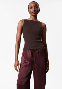 Braun geripptes Tanktop mit weitem Ausschnitt, kombiniert mit burgunderroten, satinierten, weit geschnittenen Hosen mit Kordelzug an der Taille.