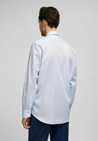 Light blue long-sleeve shirt with a button-down collar, smooth texture, and rounded hem. Features buttoned cuffs and minimal detailing.