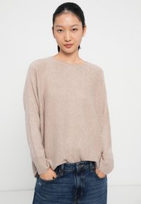 Light pink knit sweater with a relaxed fit and ribbed cuffs, paired with blue denim jeans. The texture appears soft and slightly fuzzy.
