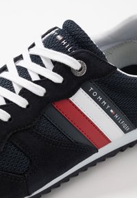 Czarne zamszowe i materiałowe sneakersy z białymi sznurówkami, z poziomymi paskami w kolorze czerwonym i białym oraz małą srebrną metką logo z boku.