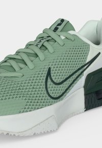 Ανοιχτό πράσινο αθλητικό παπούτσι Nike Air Max με υφή υφάσματος, μαύρο λογότυπο swoosh και λευκή μαλακή σόλα, γωνιακή προβολή για να φαίνονται οι λεπτομέρειες από το πλάι και το μπροστινό μέρος.