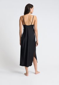 Abito lungo in satin nero con spalline sottili, spacco laterale e texture liscia. Design semplice con un aspetto elegante e minimale.