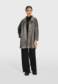 Siva jakna me mekanom teksturom, s kragnom od krzna, dugmadi na kopčanje i bočnim džepovima. Nosena preko crne majice i uparena s crnim hlačama.