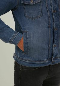 Chaqueta de mezclilla en azul oscuro con un diseño clásico, que presenta un cierre de botones en el frente, un bolsillo en el pecho y bolsillos laterales. Detalle de costura distintivo.