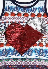 Bluzka bez rękawów z kolorowym wzorem kwiatów i ryb. Na środku widoczna duża serce wykonane z czerwonych i srebrnych cekinów.