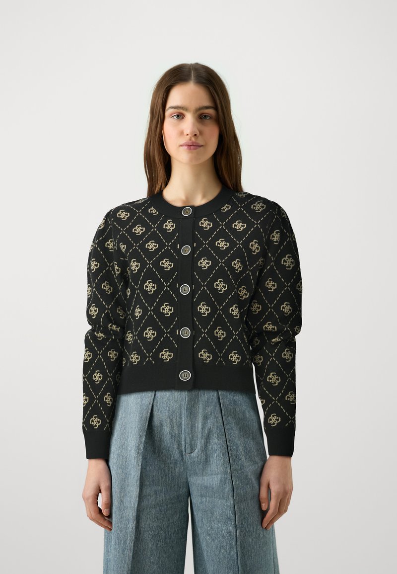 Black cardigan with a diamond pattern in beige, featuring round buttons and ribbed cuffs. Paired with light denim pleated trousers.
