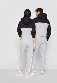 Grijze sweatshirt en joggers met zwarte accenten, voorzien van een capuchon en zijstrepen. Het materiaal is zacht; de outfit heeft een comfortabele pasvorm.