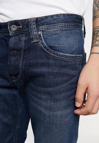 Jeans in denim blu scuro con una vestibilità dritta, tasche frontali e cuciture a contrasto. Il tessuto è liscio con una sottile texture.