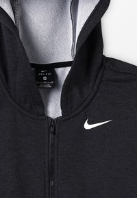 Černá mikina na zip s šedým interiérem, vyrobená z prodyšného materiálu. Na hrudi se nachází bílé logo Nike a má podšívku kapuce.