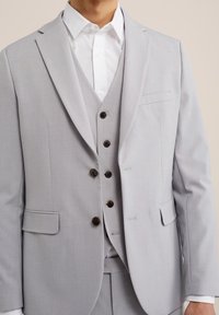 Ljusgrå kostym med notchad krage, enkelknäppt kavaj och synlig knappstängning. Tyget har en slät textur och kombineras med en vit skjorta.