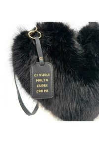 Borsa a forma di cuore in pelliccia sintetica nera con un'etichetta in pelle che presenta testo dorato. Include un anello dorato per l'attacco e una tracolla nera.