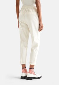 Crème katoenen broeken met een relaxed fit, elastische tailleband en opgerolde pijpen. Draag ze met gestreepte sokken en witte instappers.