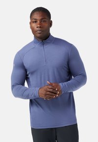 Pullover sportivo viola a maniche lunghe con scollatura a metà zip, texture liscia e design aderente, con dettagli a costine sulle spalle.