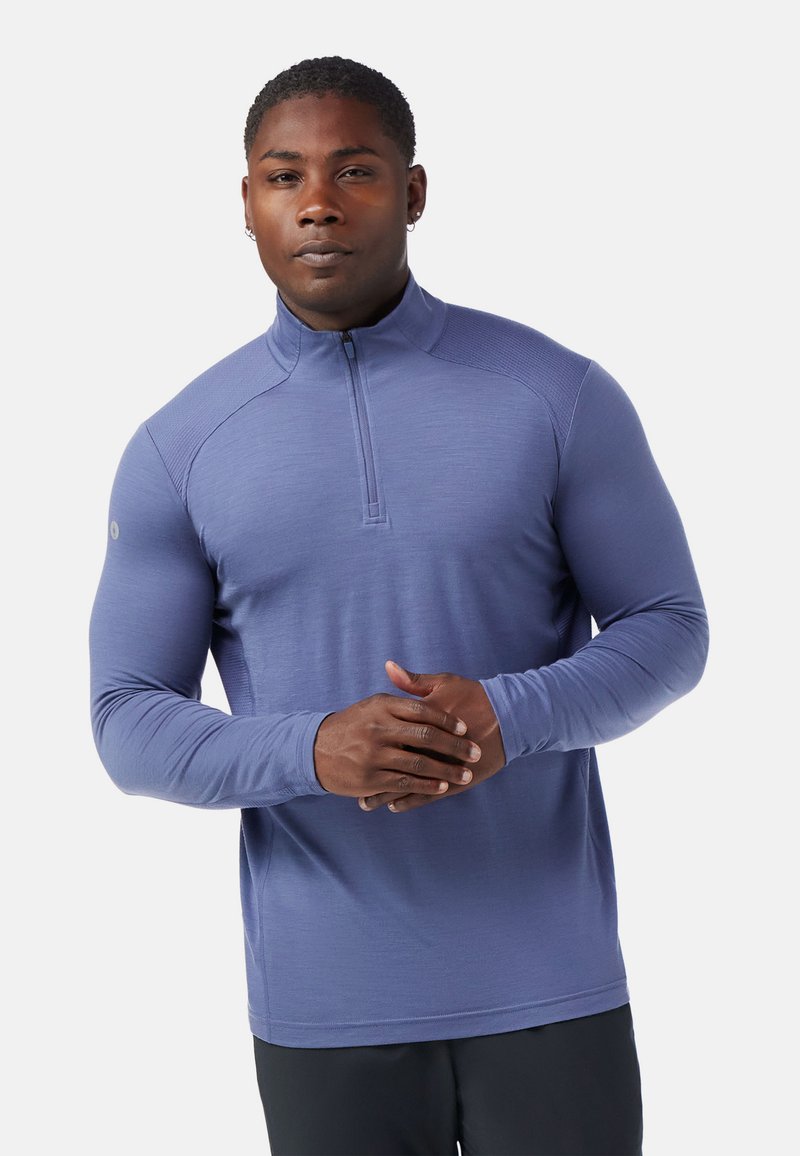 Pullover sportivo viola a maniche lunghe con scollatura a metà zip, texture liscia e design aderente, con dettagli a costine sulle spalle.