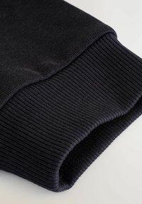 Schwarzer gerippter Bund eines Sweatshirts, mit glatter Textur und leichtem Glanz, gefaltet mit sauberen Kanten und gleichmäßiger dunkler Farbgebung.