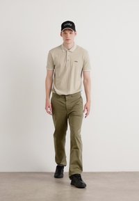 Beige polo shirt with contrasting collar, olive green pants, and black sneakers. Black cap with logo. Simple and casual outfit.