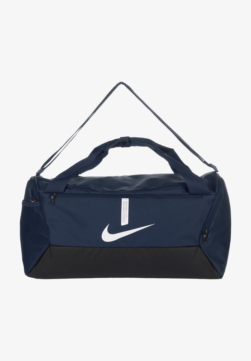 Tummansininen matkakassi mustalla pohjalla, vetoketjukiinnitys, kaksinkertaiset kantokahvat ja valkoinen Nike-logo edessä.