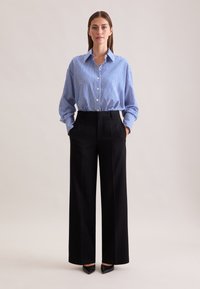 Camicia a righe blu e bianche con colletto, abbinata a pantaloni neri a vita alta e gamba larga e tacchi a punta neri.