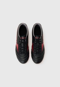 Zapatillas deportivas negras y rojas, con una parte superior de cuero liso, puntera redondeada, patrones texturizados y cordones negros sobre un interior gris.