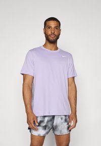 Lilac Nike T-shirt with short sleeves and crew neckline. Features a small white logo on the chest. Worn with gray and black patterned shorts.