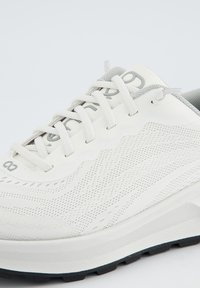 Weißer Sportschuh mit Obermaterial aus Mesh, strukturiertem Oberflächen und grauen Akzenten. Verfügt über Schnürsenkel und eine gepolsterte Sohle zur Unterstützung.